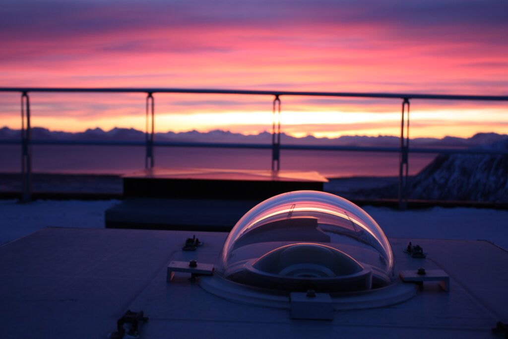 Sunset, pinkish colored clouds in the background, with a transparent instrument dome in the foreground.